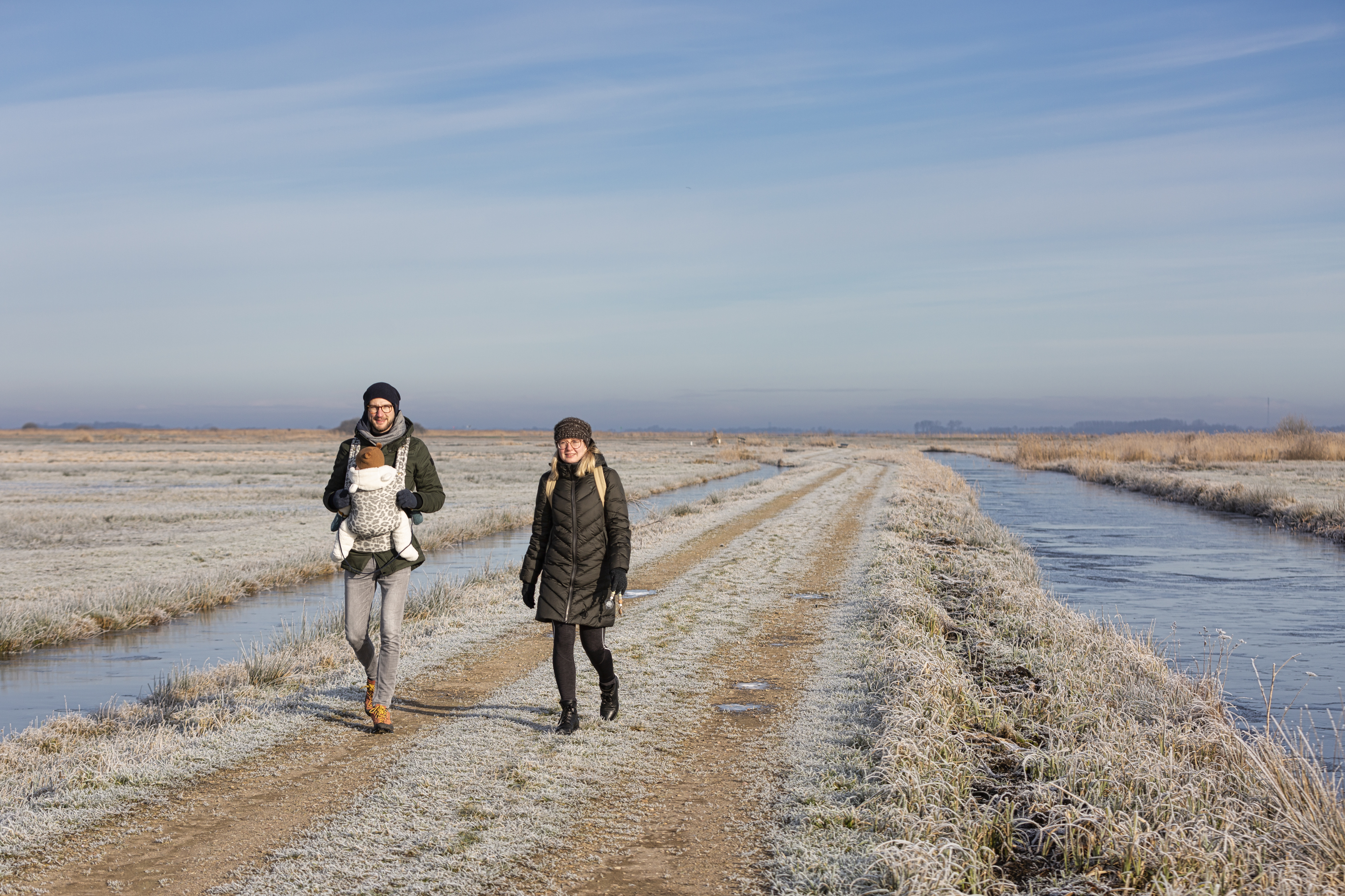 Duo met baby wandelend tussen twee sloten in winterse omstandigheden
