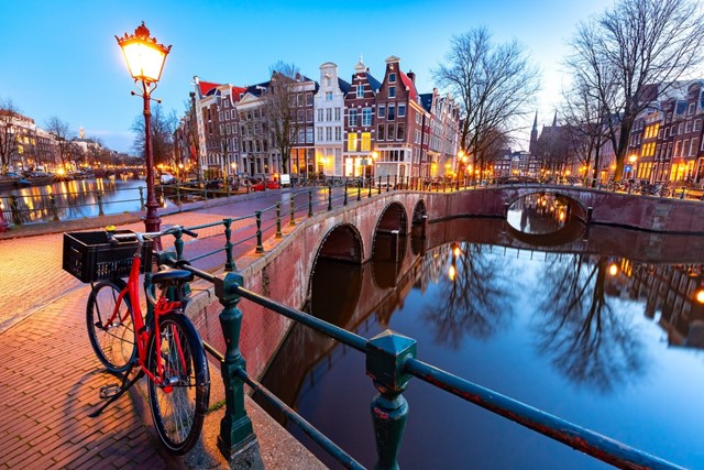 afbeelding van een sfeervol verlichte brug en gracht in Amsterdam in de avond.