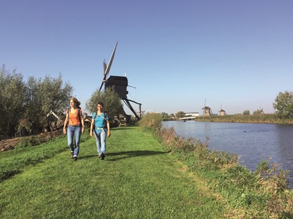 Duo wandelend langs het water met een molen op de achtergrond