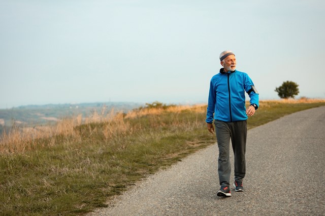 man met hoofdband die buiten in de natuur wandelt met een koptelefoon om zijn nek.