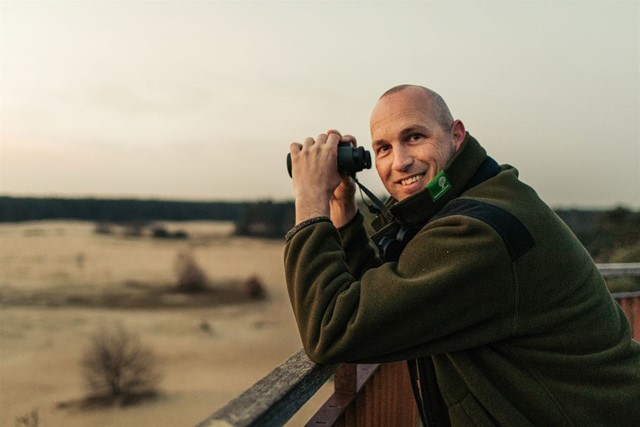 afbeelding van boswachter Laurens met een verrekijker in zijn handen, op de Veluwe.