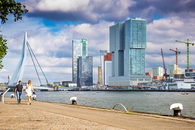 wandelaars an de Rotterdamse boulevard met wolkenkrabbers en brug op de achtergrond.