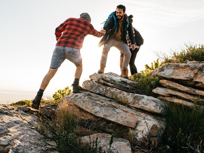 afbeelding van wandelaars die elkaar helpen naar de top van een berg.