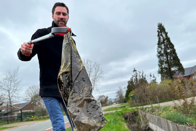 man met afvalgrijpstok laat afval zien dat hij heeft gevonden op straat.