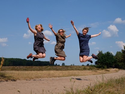 drie vrouwen springen in de lucht in hun wandeljurkjes.