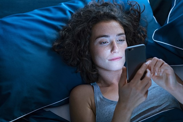 afbeelding van een vrouw die 's avonds op haar telefoon kijkt.