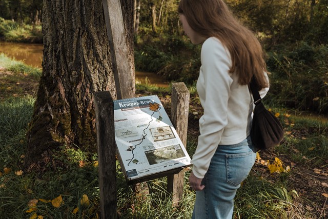 Vrouw kijkt op informatiebord over het grensgebied tijdens haar wandeling
