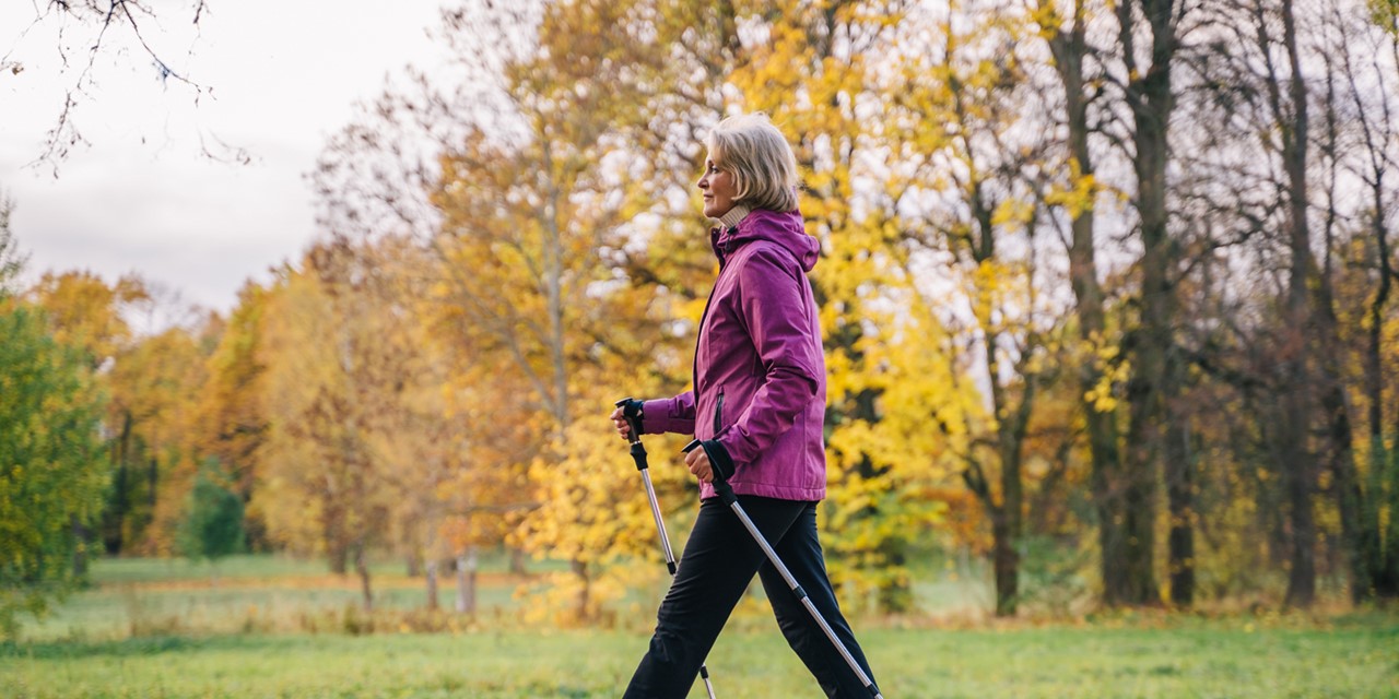 vrouw wandelt met wandelstokken in een park.