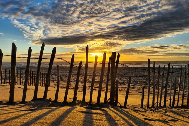 zonsondergang op het strand met een hekje met houten palen.