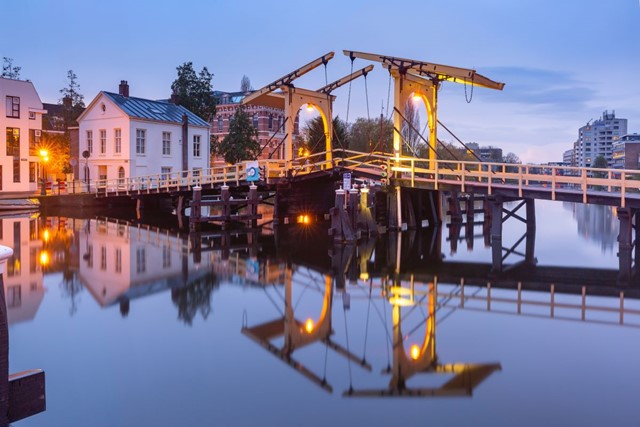 afbeelding van een sfeervol verlichte brug en gracht in Leiden in de avond.