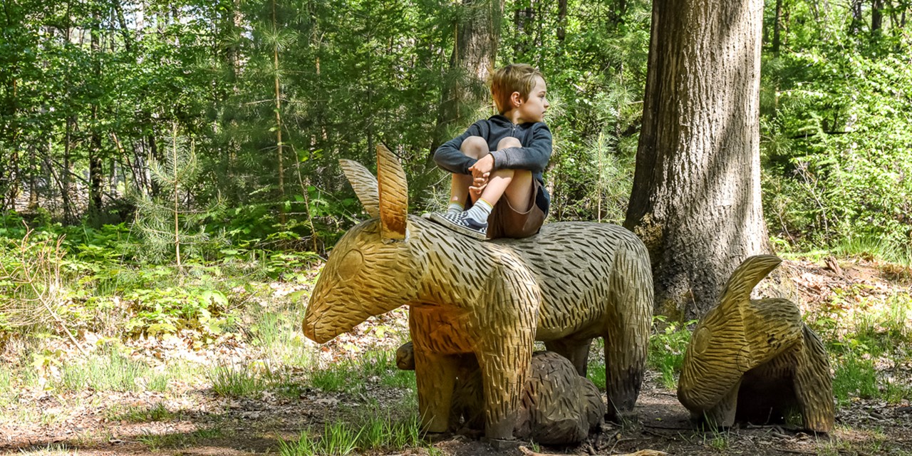 jongen zit op een beeld van een dier in het bos.