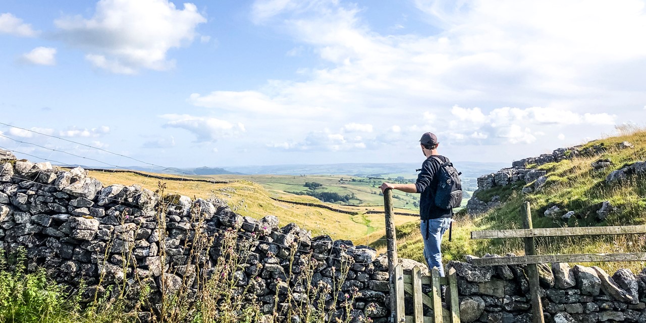 een wandelaar kijkt uit over het weidse landschap in Malham North Yorkshire.