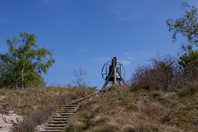 trap in de duinen leidt naar een grote bel.