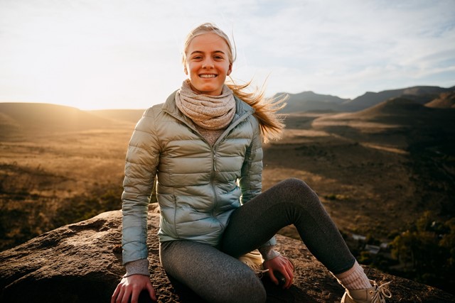 Jonge vrouw draagt een grijze wandeljas en poseert voor de camera