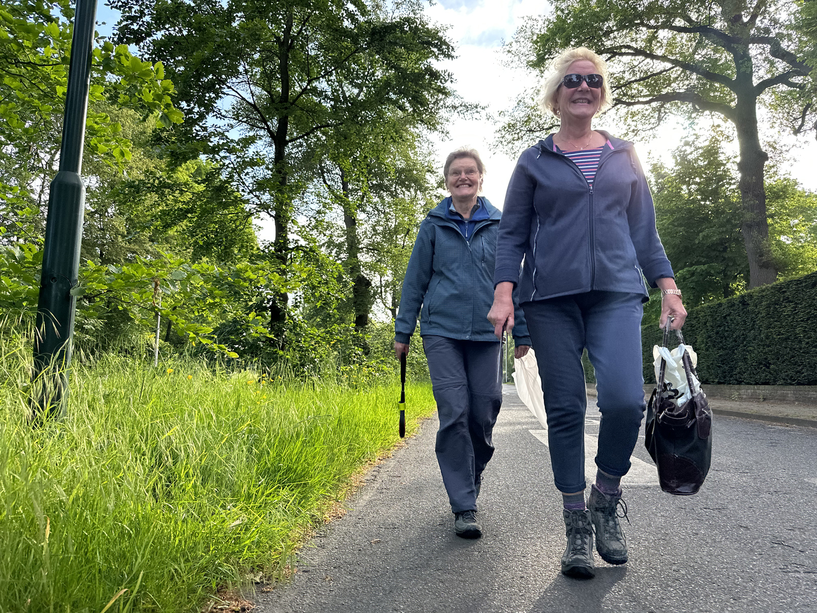 twee vrouwen plandelen met een grijpstok en vuilniszak op straat.
