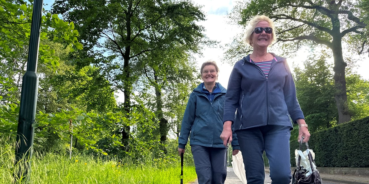 twee vrouwen plandelen met een grijpstok en vuilniszak op straat.