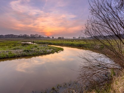 afbeelding van een rivier in het graslandschap met zonsondergang.