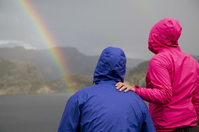 Vrouwen in regenjas kijken naar een regenboog die start in het water