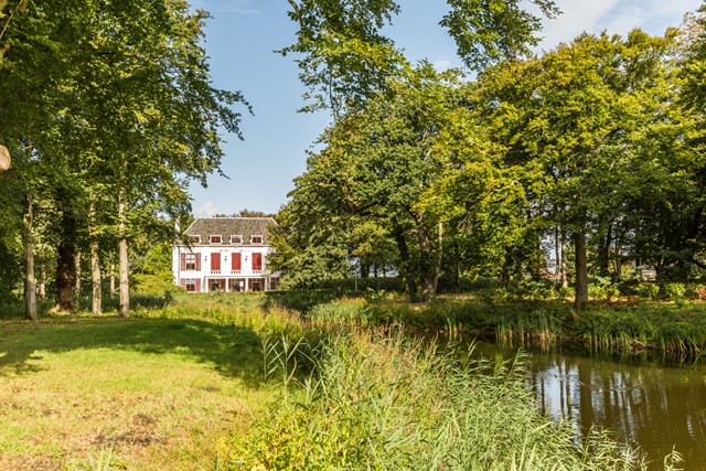 landhuis met grasveld en bomen aan het water.
