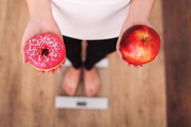 een donut en een appel, vastgehouden door iemand op een weegschaal.