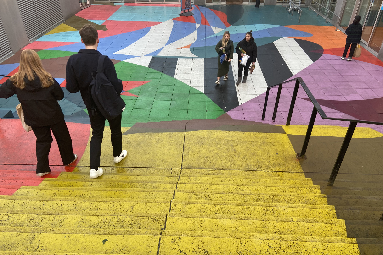 afbeelding van wandelaars op een pleintje met geverfde trappen.