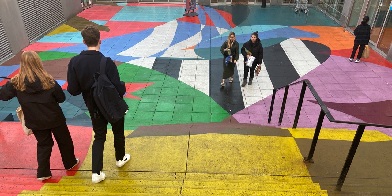 afbeelding van wandelaars op een pleintje met geverfde trappen.
