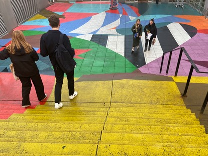 afbeelding van wandelaars op een pleintje met geverfde trappen.