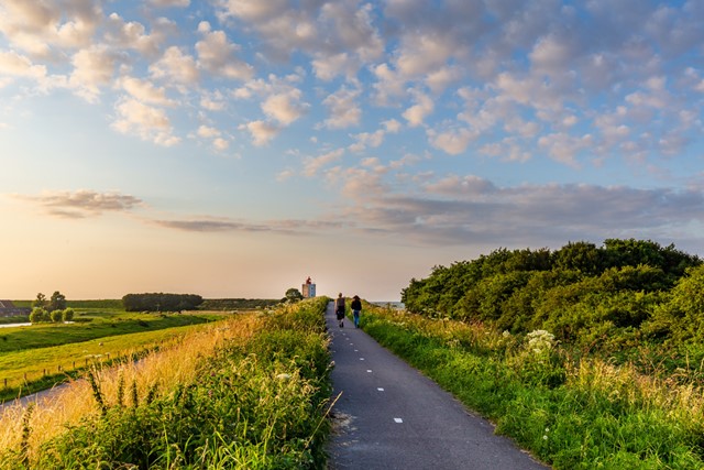 afbeelding van twee wandelaars in een zonnig Nederlands landschap.