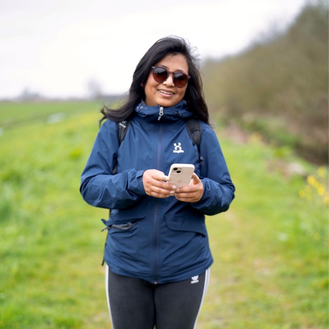 vrouw met oogproblemen wandelt met telefoon in haar hand en zonnebril op.