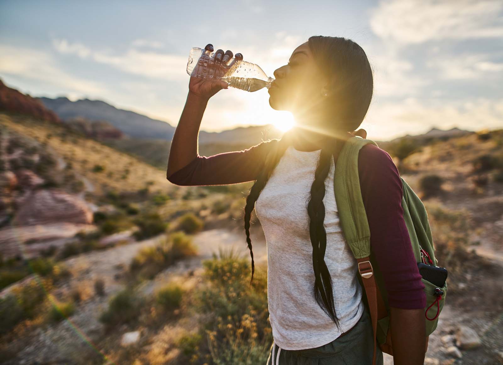 foto van een vrouw die uit een flesje drinkt in de zon.
