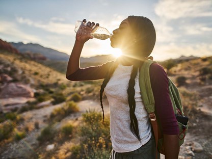 foto van een vrouw die uit een flesje drinkt in de zon.