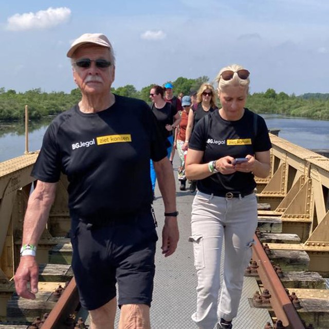 Henk Schilder en meerdere wandelaars lopen over een brug.