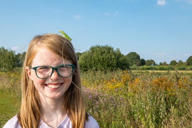 Agnes met een groene sprinkhaan op haar hoofd.