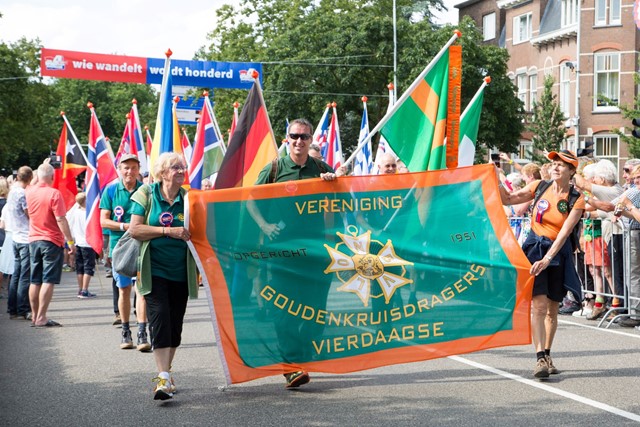 4Daagselopers wandelen met een vlag van de Vereniging Gouden Kruisdragers.
