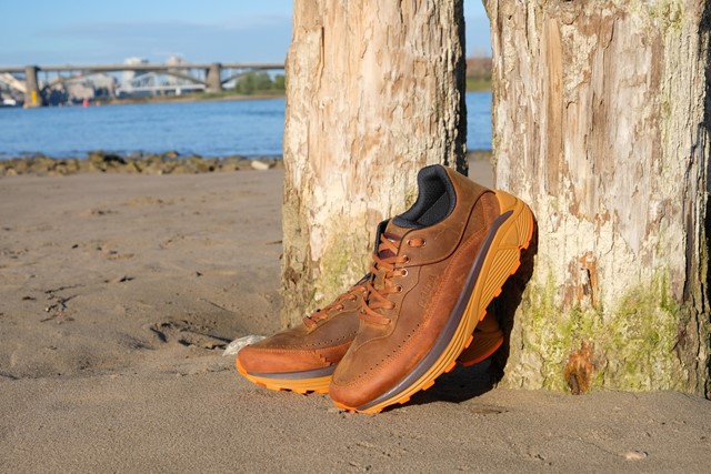 afbeelding van DUCA-wandelschoenen op een zandstrand, tegen houten palen.