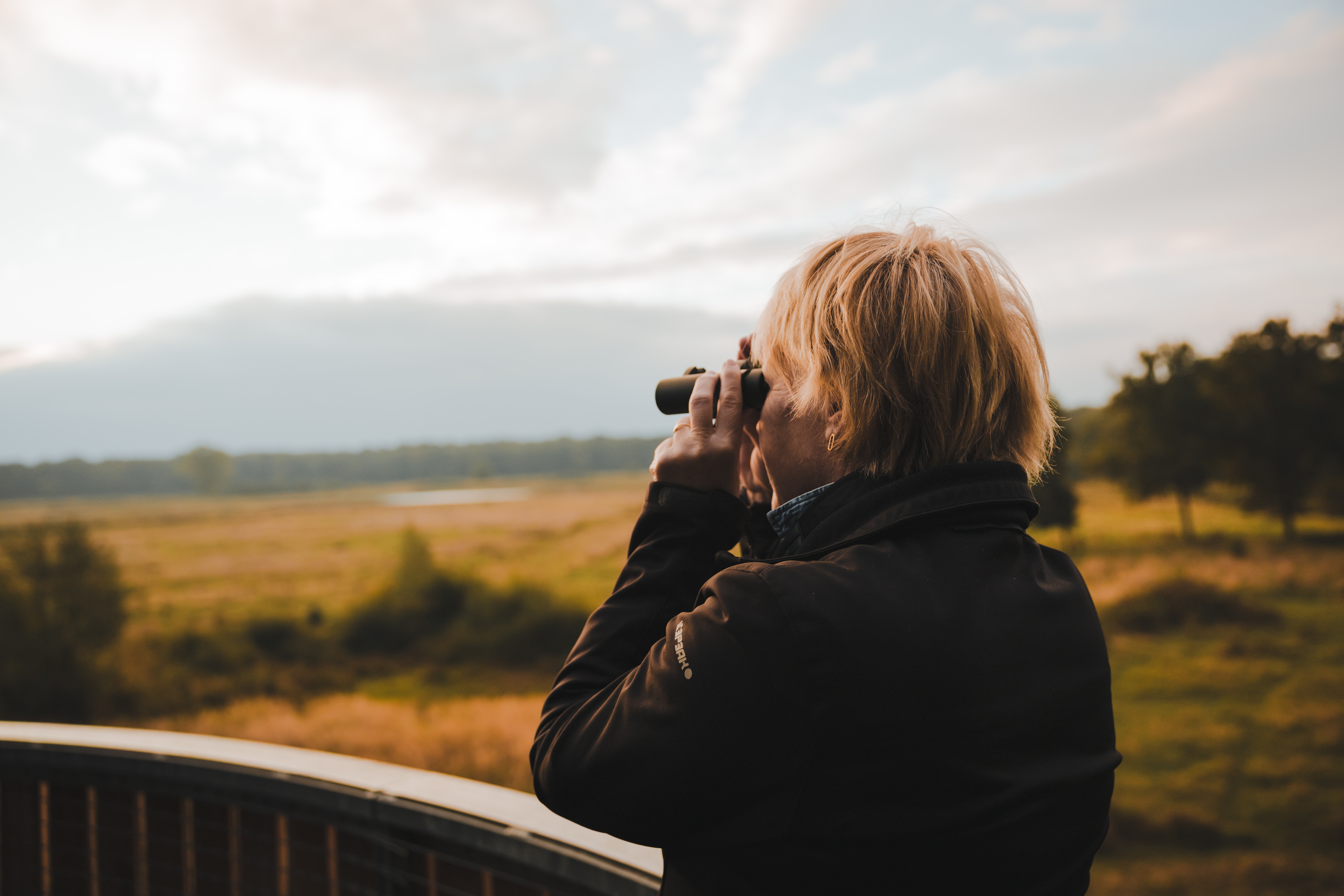 Vrouw kijkt met verrekijker uit over het landschap van Hart van Limburg 