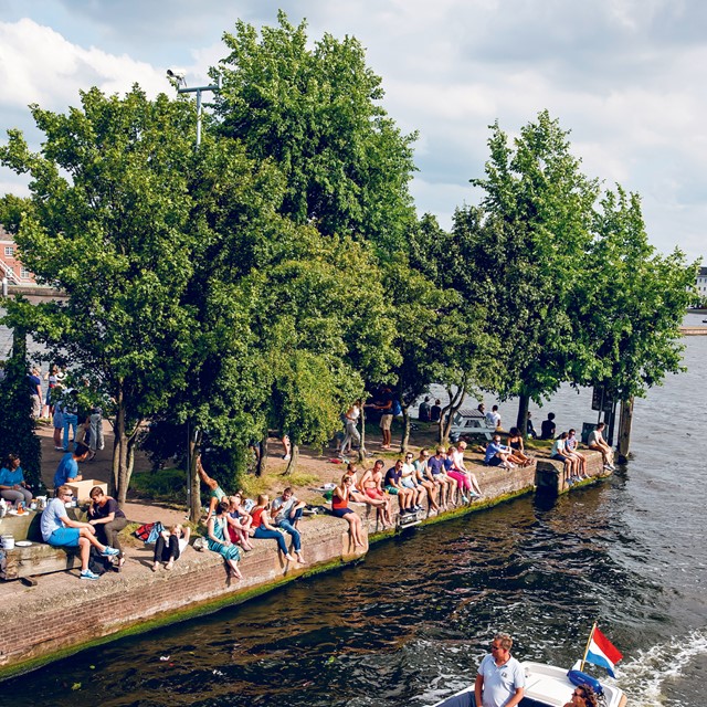 afbeelding van mensen die met hun benen langs het water bungelen op het terras van Hannekes Boom.