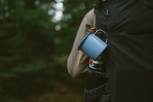 een mok, een drinkfles en andere bepakking tijdens een trektocht in het bos.