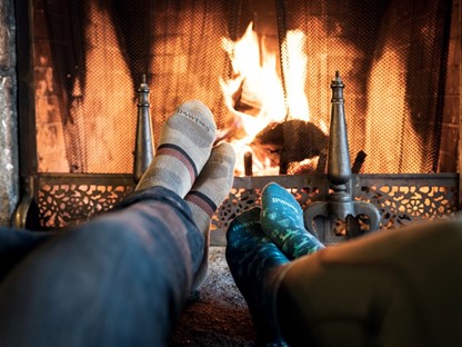 afbeelding van twee mensen die hun voeten opwarmen bij het vuur van de open haard.