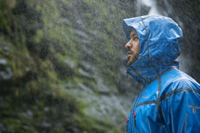 Man in regenjas wandelend in de regen