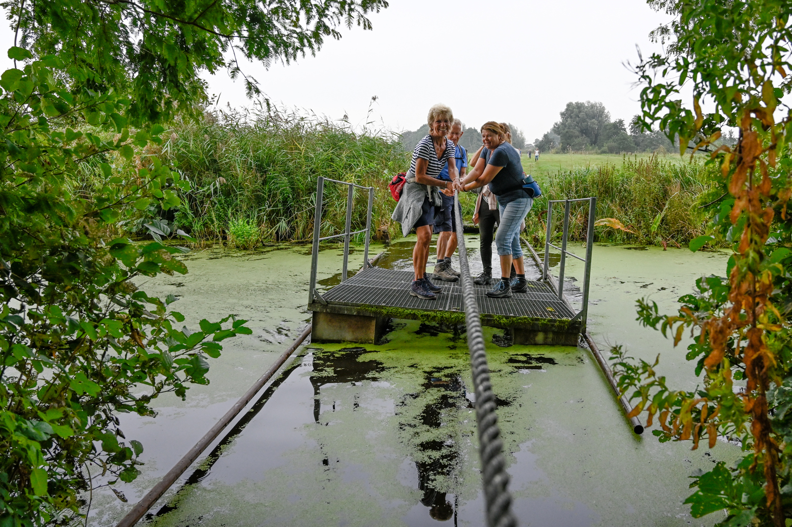 Wandelaars gaan met een trekpontje een sloot over tijdens de Otterloop.