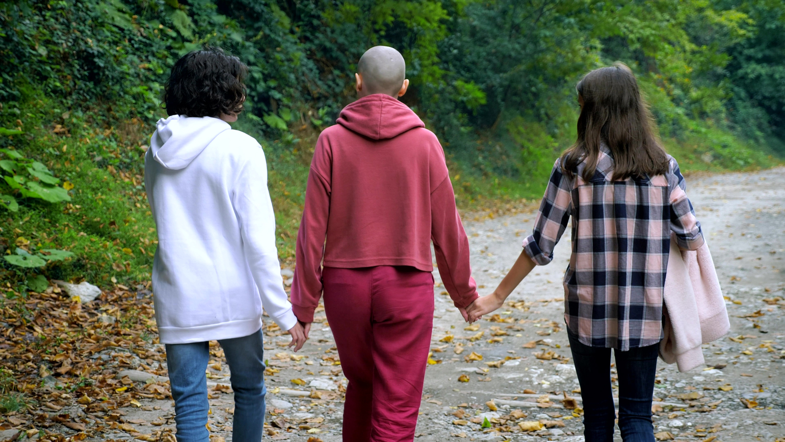 moeder loopt met kaal hoofd in de natuur met twee kinderen aan haar zijde.