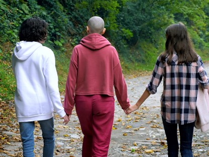 moeder loopt met kaal hoofd in de natuur met twee kinderen aan haar zijde.