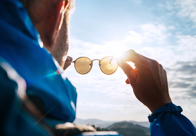 Man houdt zonnebril in zijn hand en wijst ermee naar de zon 